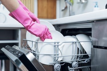 housewife taking out clean dishware from dishwasher at home kitchen